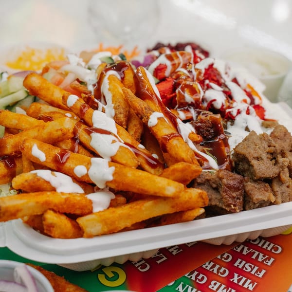Halal Munchies platter with seasoned fries, chicken, lamb, and salad, drizzled with white and brown sauces.
