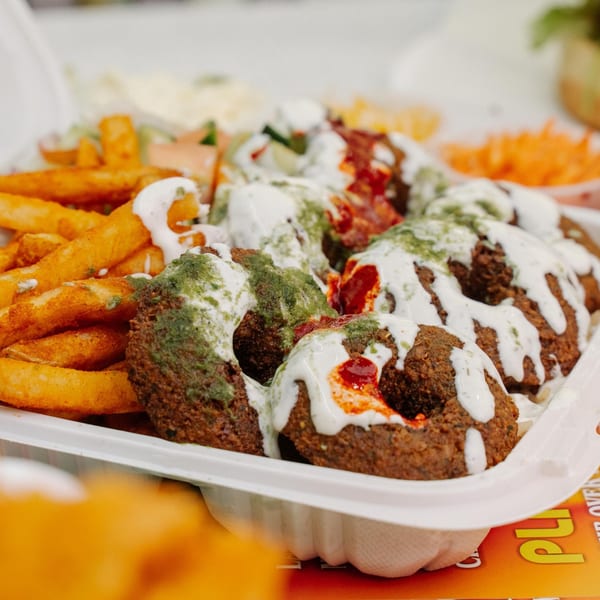 Halal Munchies falafel with white and green sauces, fries, and salad in a white container.