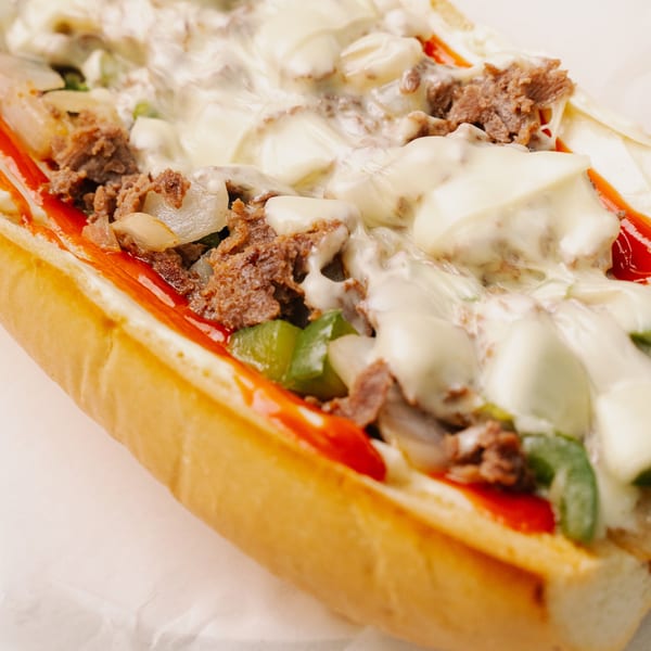 Close-up of a Halal Munchies cheesesteak with melted cheese, steak, peppers, and onions.